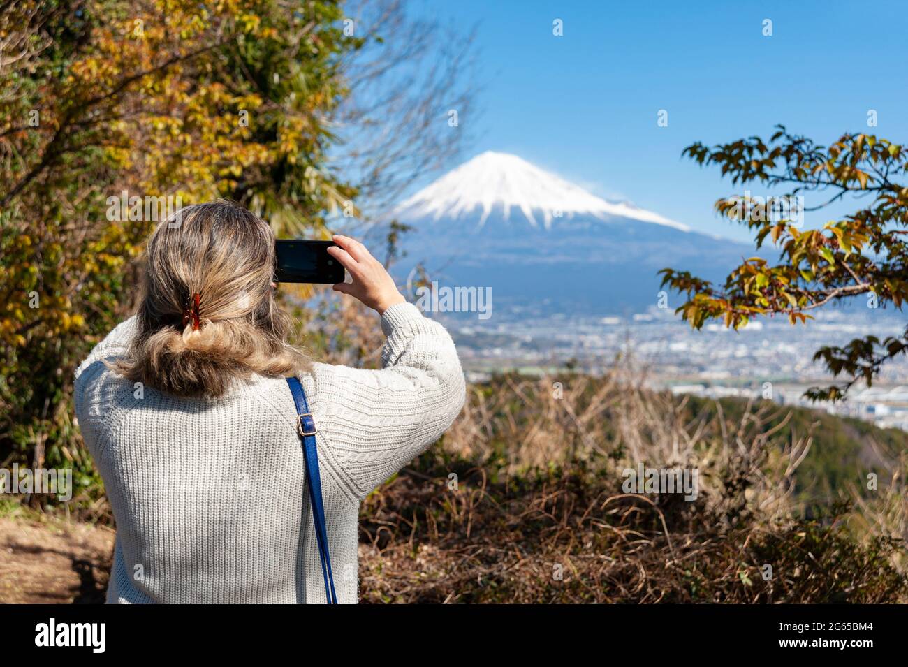 Woman taking a photo of Mount Fuji, with an aerial view of Fuji City. Photo taken from Noroshiba, Kanbara, Shimizu Ward, Shizuoka Ken. Stock Photo