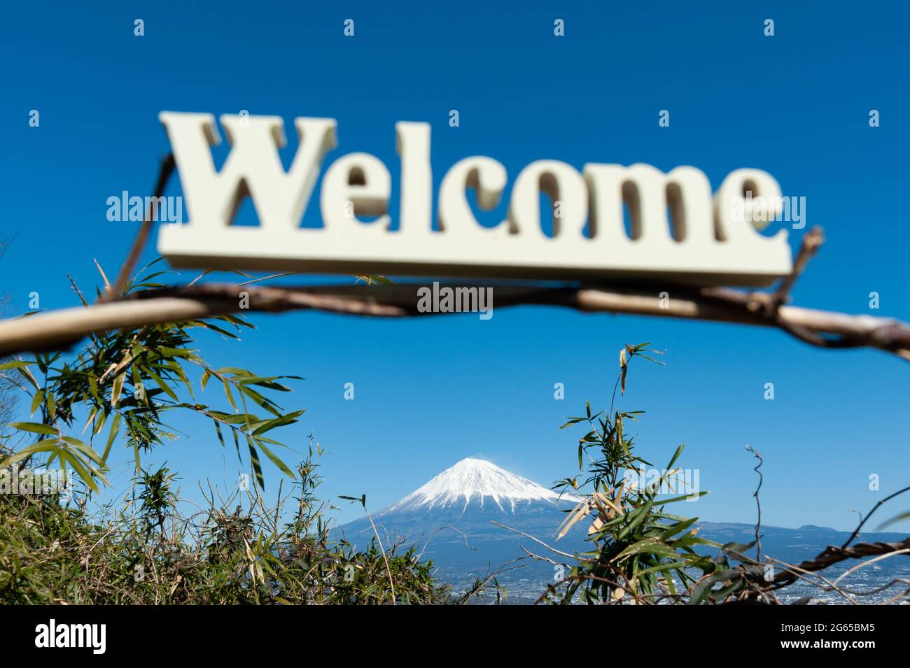 'Welcome' word written in wood. Background with Fuji City aerial view and the famous Mount Fuji with snowy peak. Stock Photo