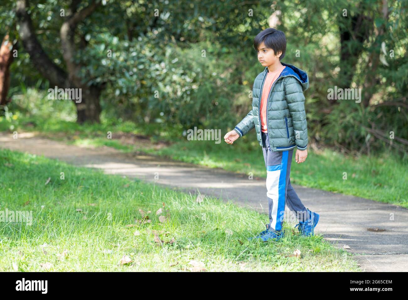 Portrait of kid walking in the park in sunlight. Greenery in the background. Stock Photo