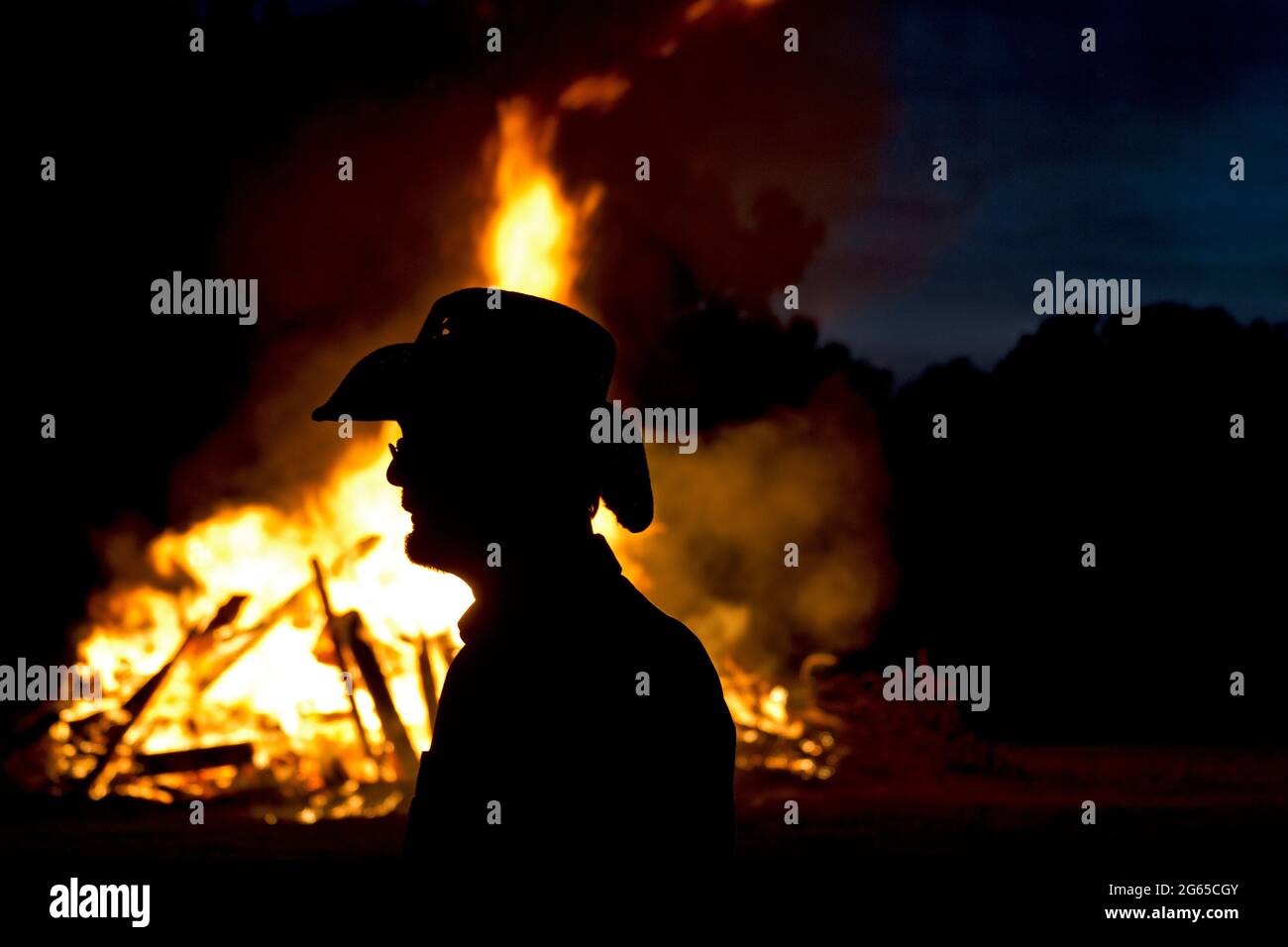 A fire burns behind the silhouette of a man. Stock Photo