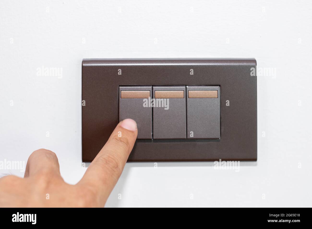 Close up fingers is turning on or turning off the brown lightswitch on stenciled white wall