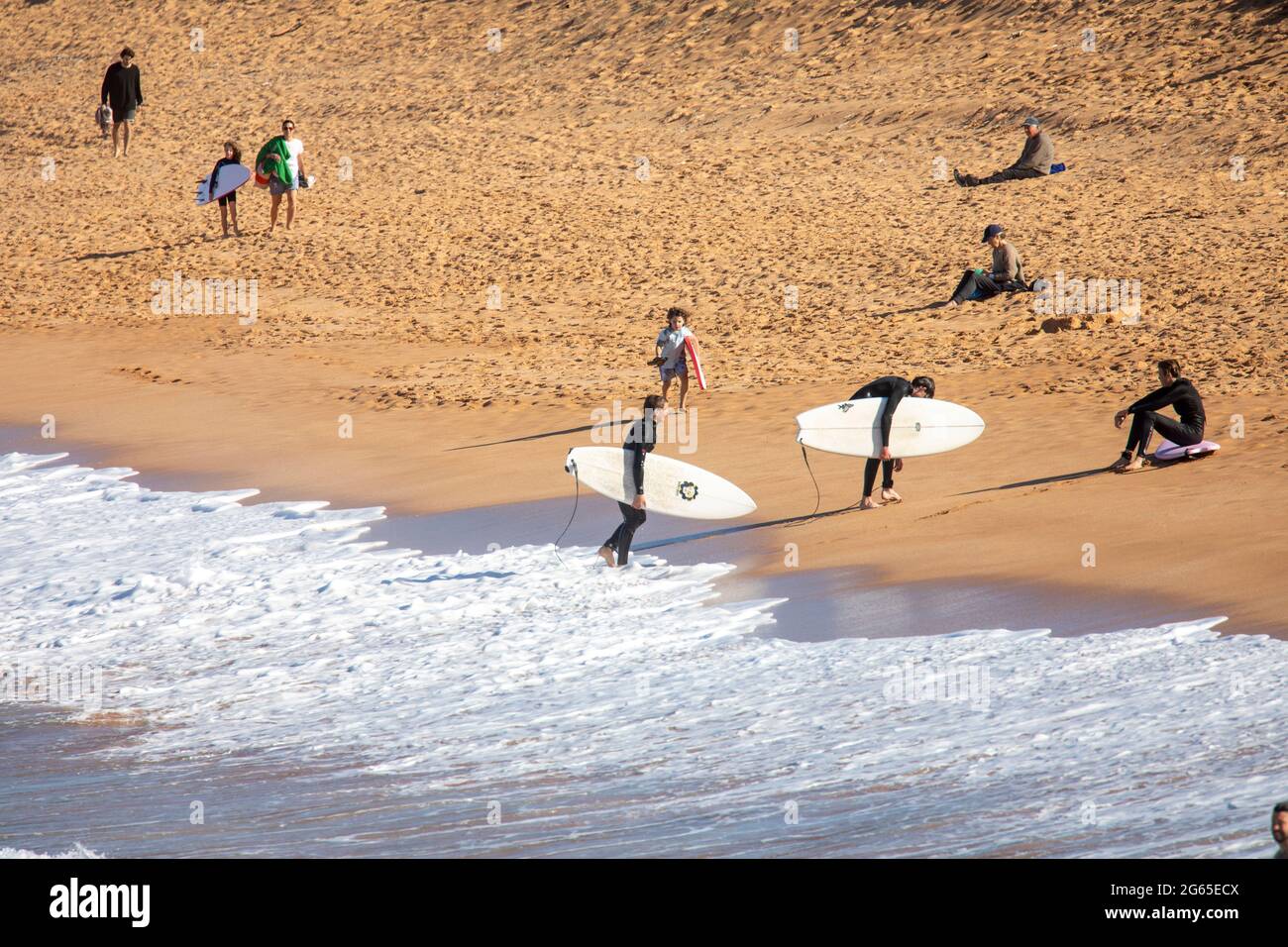 Australian male surfers carry their surfboards on Avalon Beach in Sydney on a sunny winters day