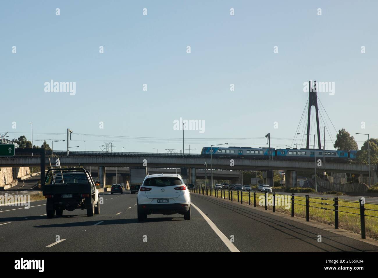 Cars on eastlink highway interchange with metro train passing overhead bridge. Stock Photo