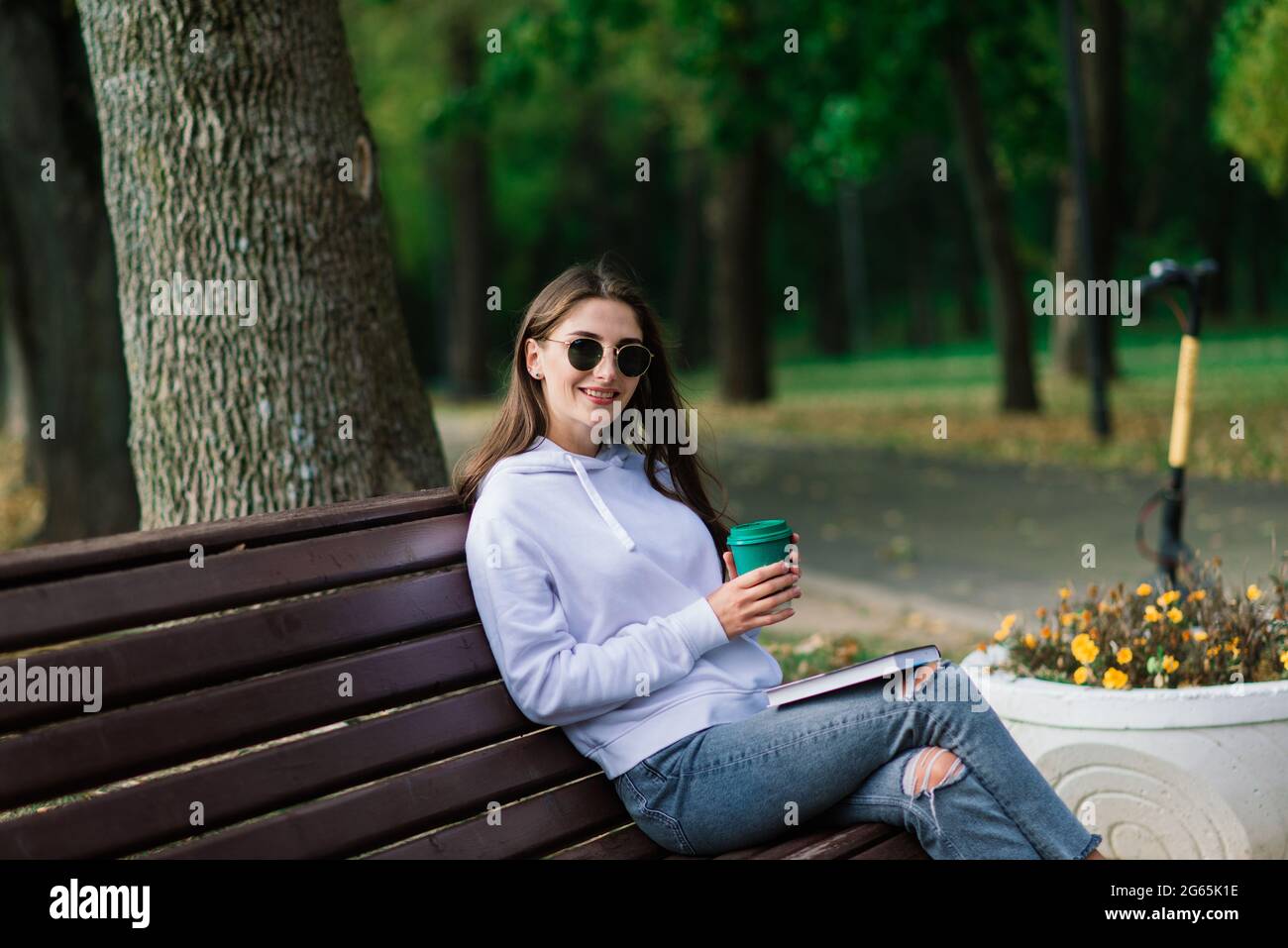 Young woman riding scooter in park sitting on a bench Stock Photo - Alamy