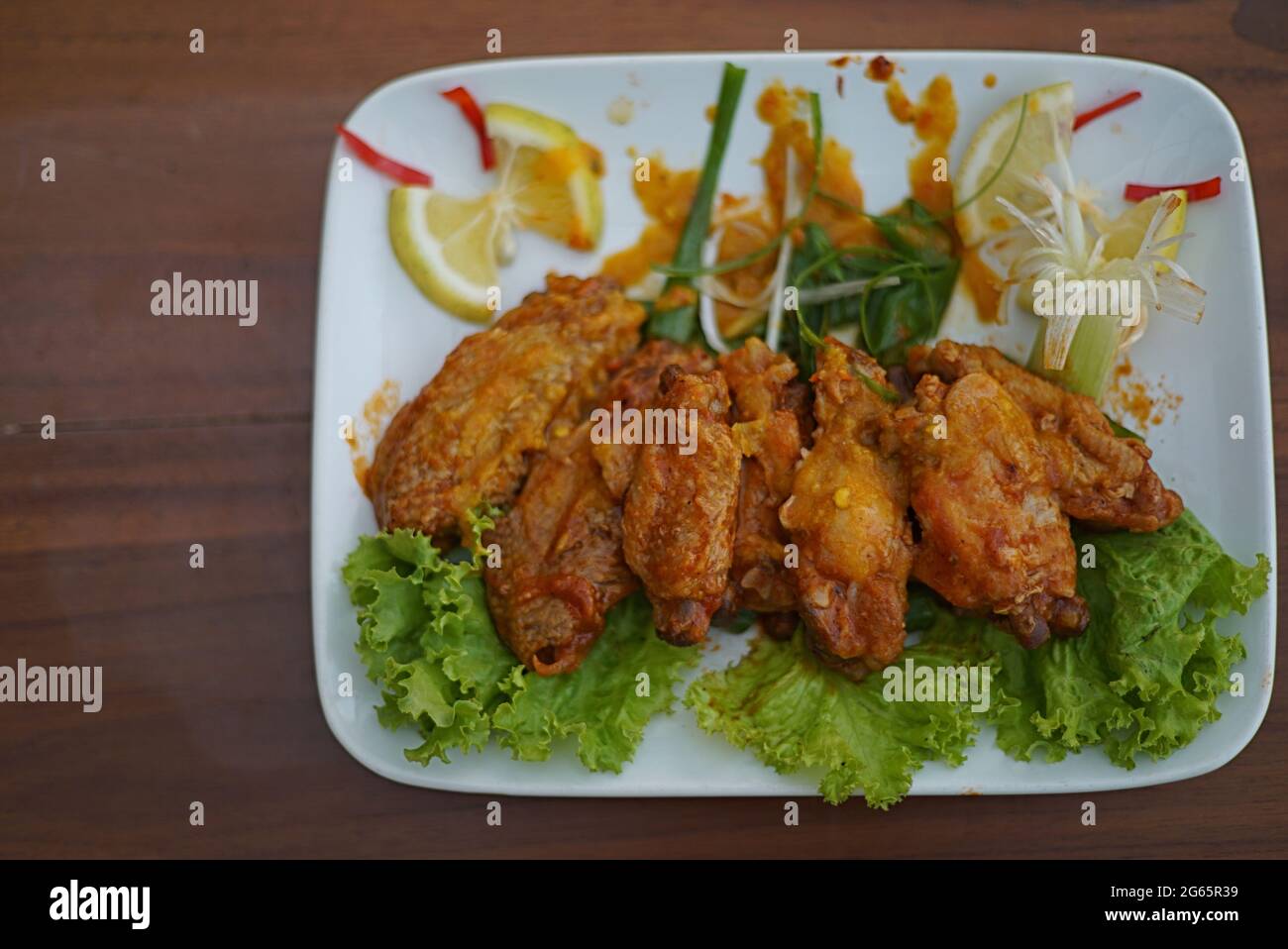 Delicious fried chicken butter in white plate. Chili and lime slice as garnish. Indonesian cuisine. Stock Photo