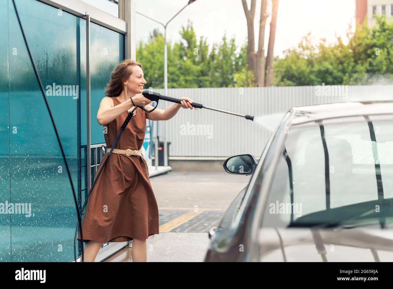 Side view young adult woman washing car with high pressure water