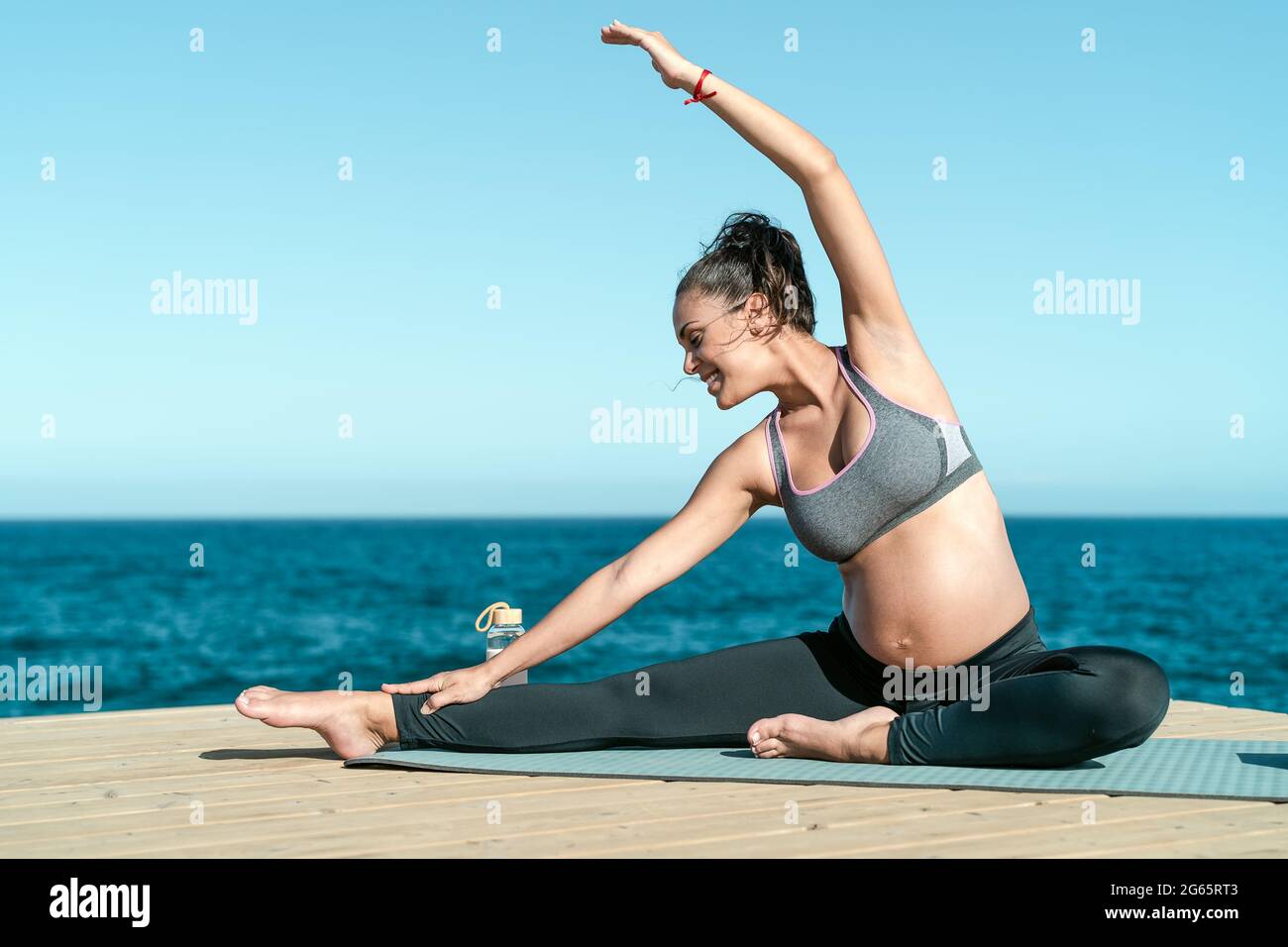 Young pregnant woman doing prenatal pilates exercises session next the sea - Health lifestyle and maternity concept Stock Photo