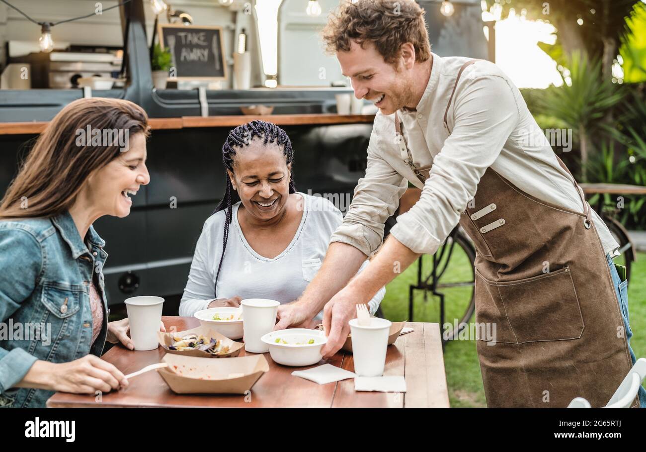 Young Food truck owner serving meal to customers table - Happy multiracial females having fun lunching together Stock Photo