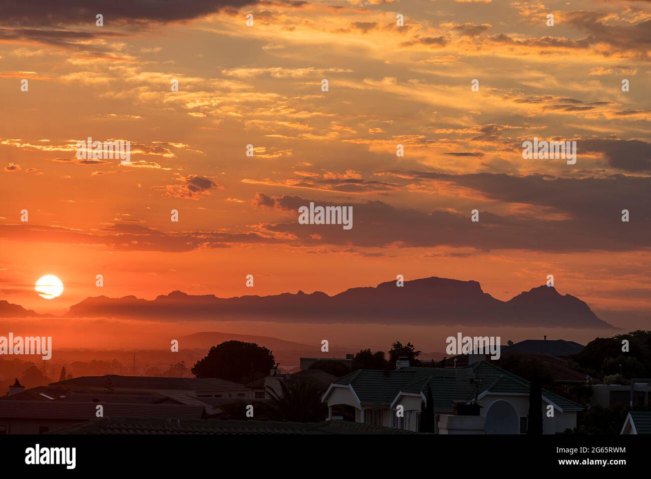 The sun is setting behind Fish Hoek accross False Bay. The back of Table Mountain and Devils Peak are visible Stock Photo