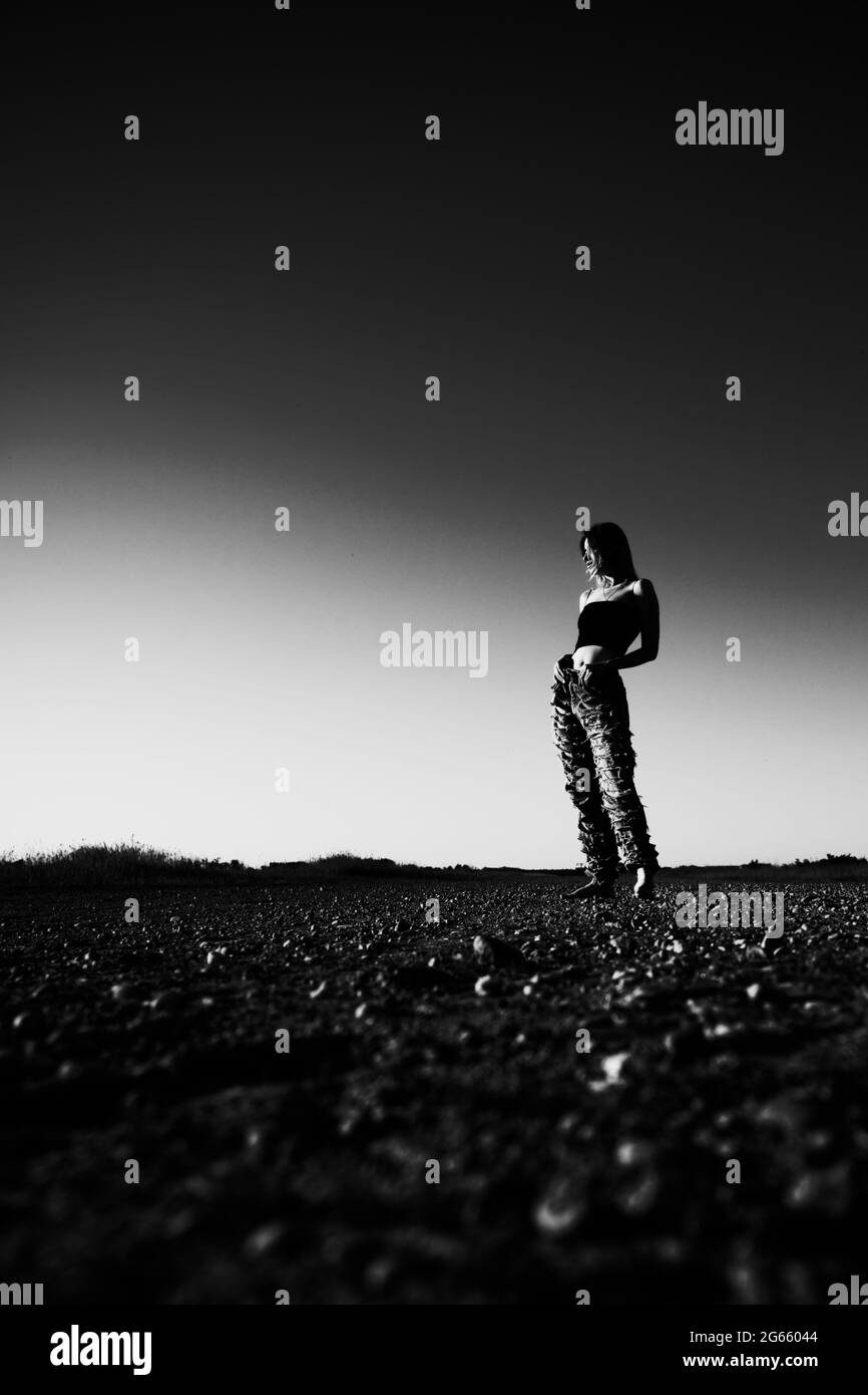 single sad tramp girl in torn jeans stand on a deserted road, monochrome Stock Photo