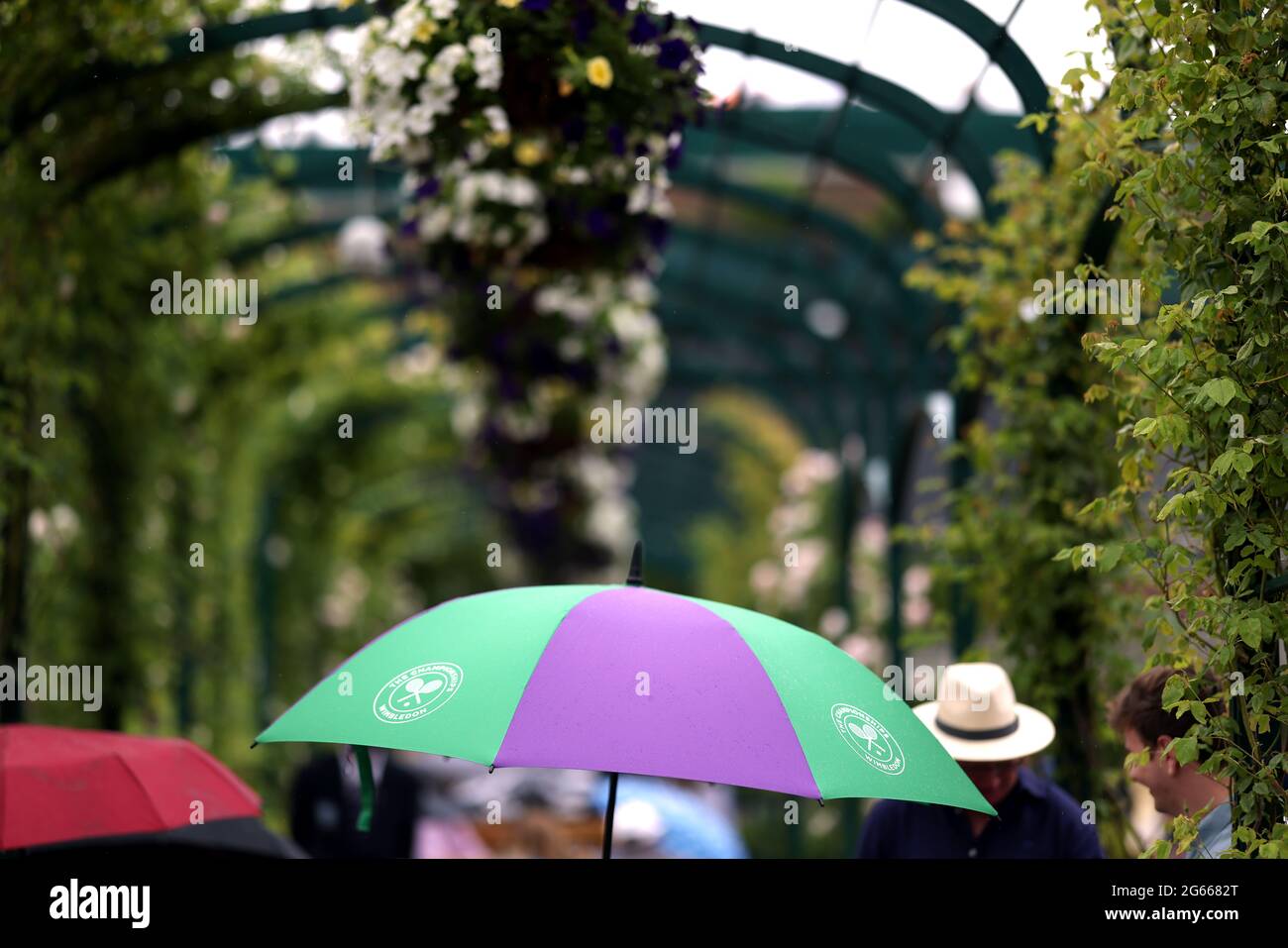 A spectator shelters from the rain under an official Wimbledon umbrella