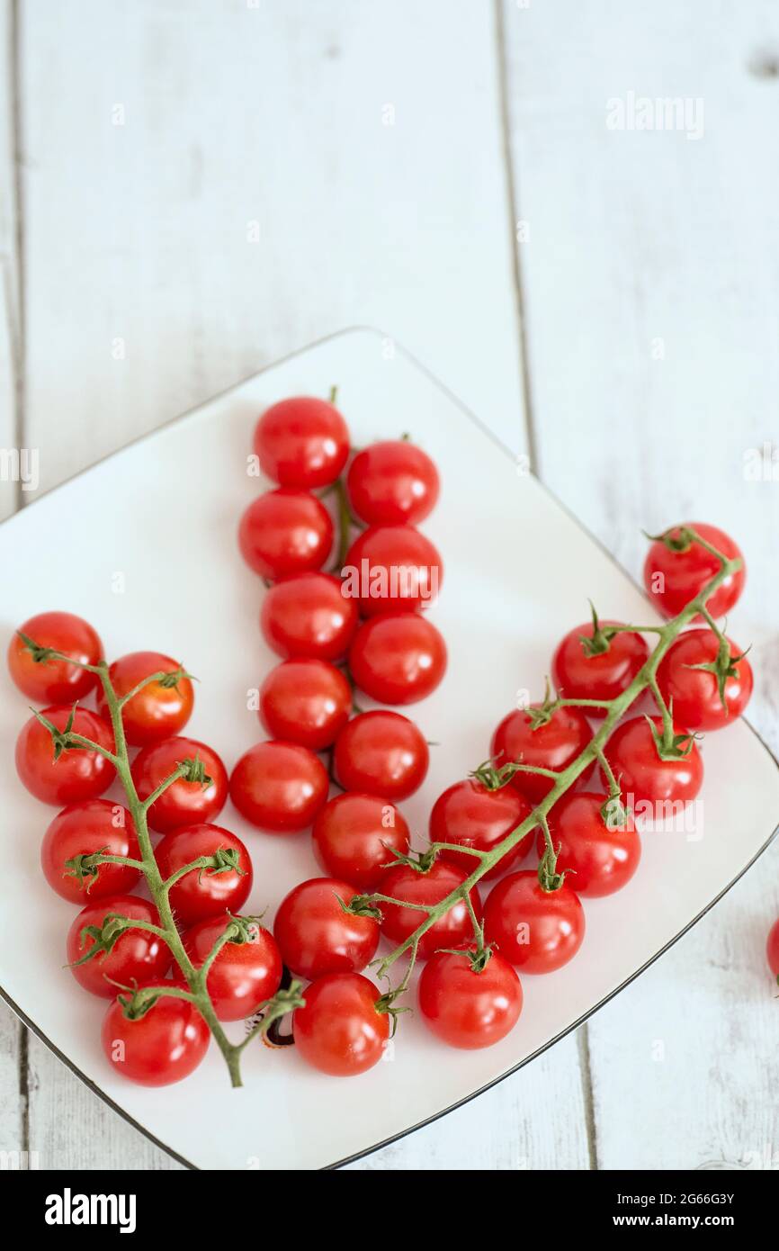 Red Cherry Tomatoes On A White Plate And White Wooden Table. Fehraltorf, Switzerland Stock Photo