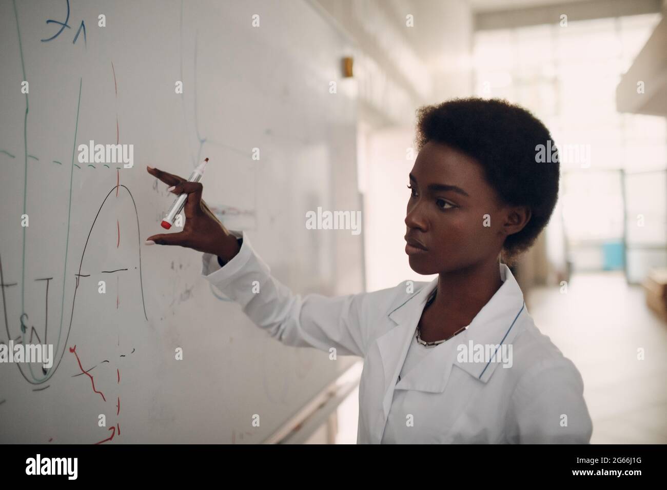 African American woman math teacher writing on blackboard with marker. Stock Photo