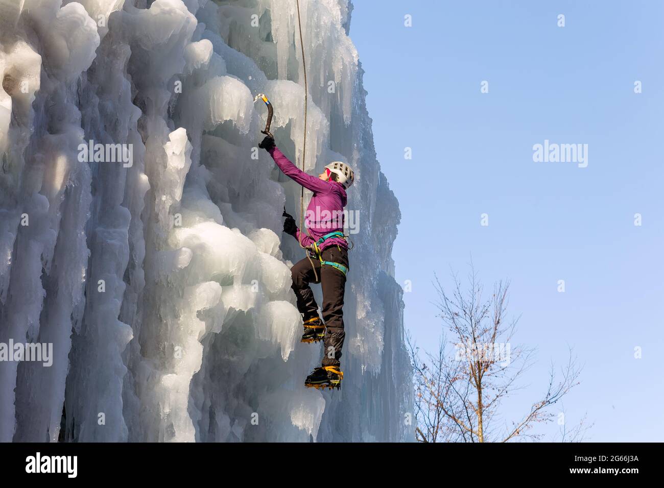 Female ice climber hiking a frozen waterfall, pushing axe pick into the ...