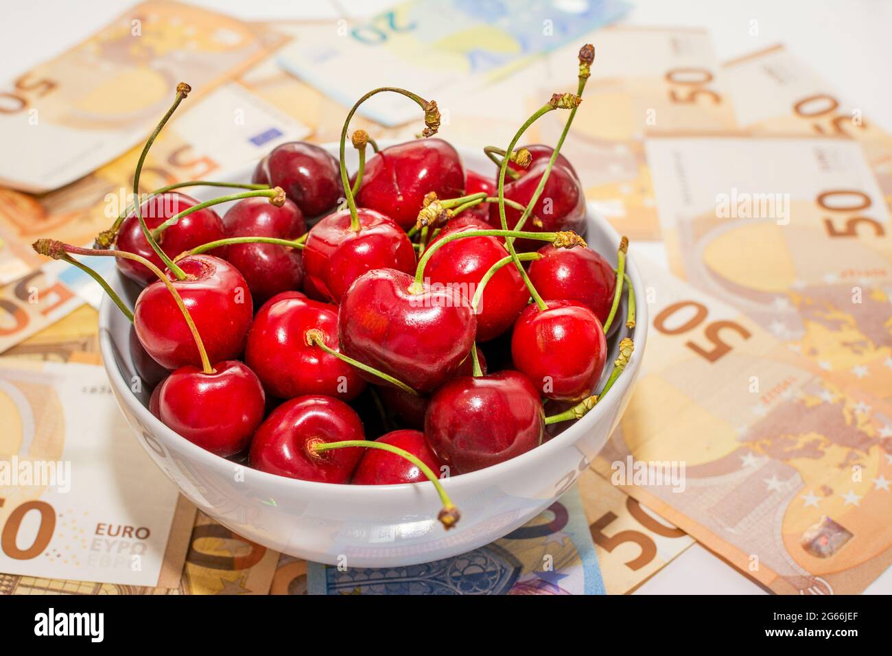 cup of cherries on a carpet of banknotes, concept of the increase in fruit prices Stock Photo