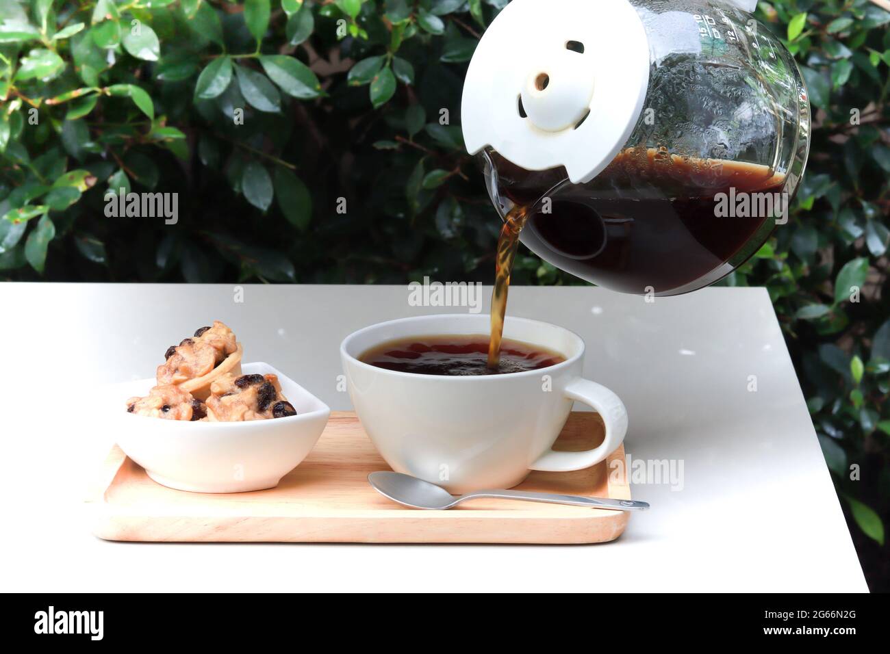 Pour coffee from pot into cup. Coffee cup served on wood tray alongside with cookies. Table set