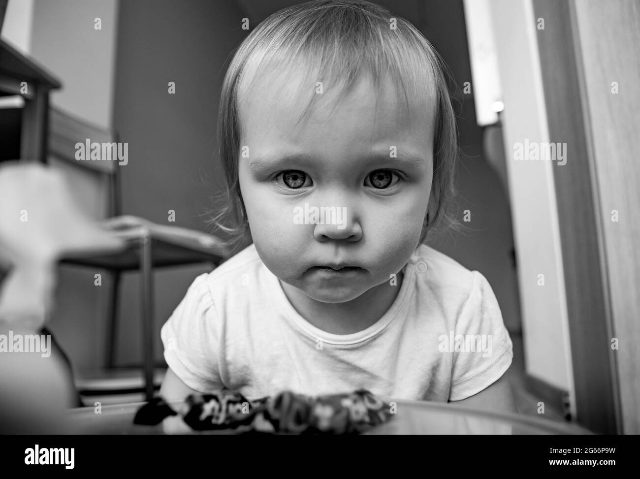 A beautiful little caucasian girl seriously looks into the frame with big eyes. Portrait of a child in black and white. Stock Photo