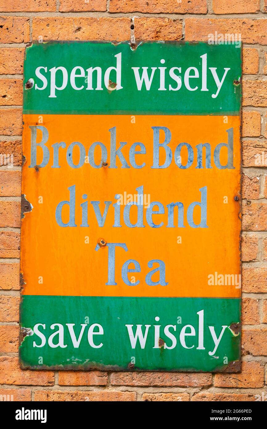 Antique Tinplate advertising sign on a brick wall, for Brooke Bond Dividend Tea. Spend wisely, save wisely Stock Photo