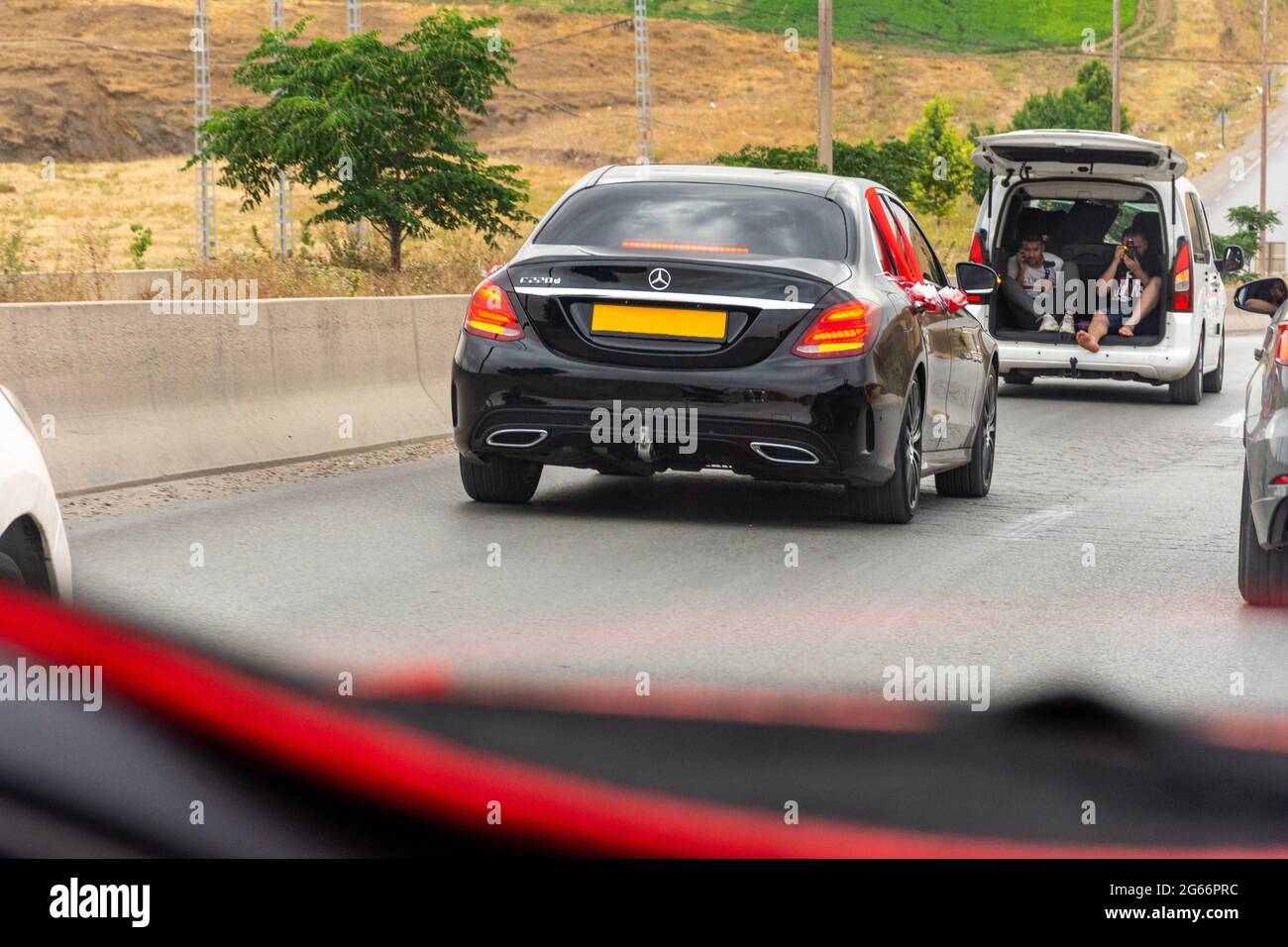 ar front window view of a black wedding car on the highway with red organza fabric and ribbon bow. Stock Photo