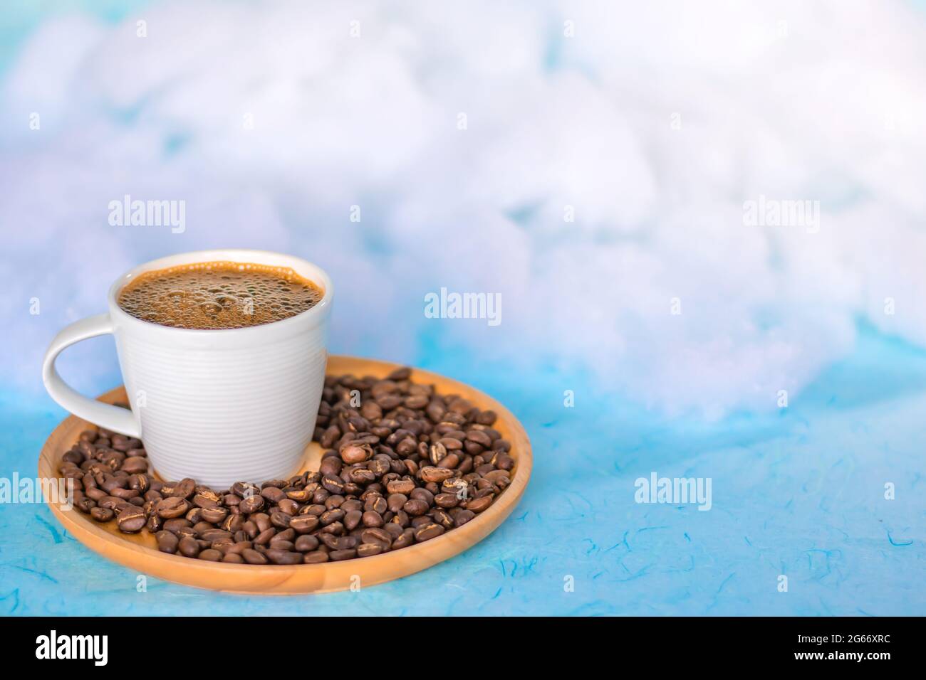 Cup of coffee and coffee beans on a round wooden tray, floating in the sky with white clouds. Copy space. Stock Photo