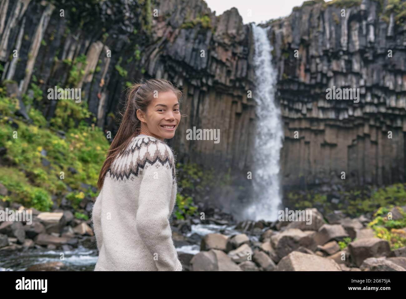 Portrait of woman on Iceland. Hiker enjoying Svartifoss waterfall. Female is visiting famous tourist attraction of Iceland. Natural landmark on Stock Photo
