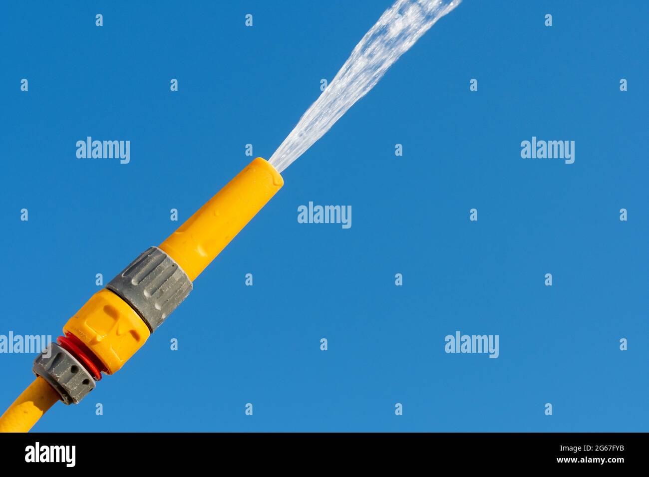 Water spraying out of a hosepipe against a clear blue sky, UK. Stock Photo