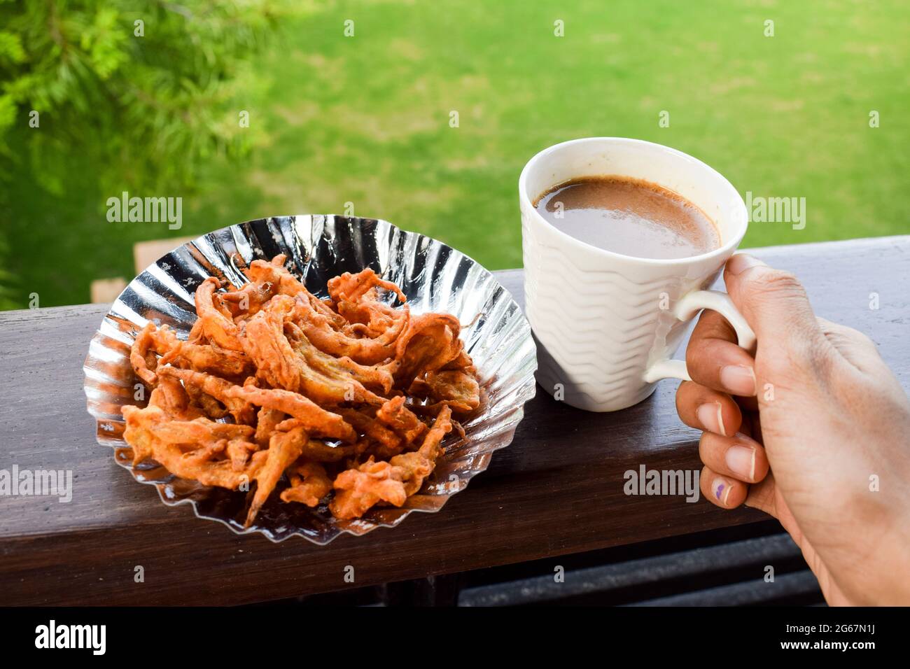Female eating and drinking Indian snacks Onion pakoda made from gramflour and deep fried. Tea time famous crispy snacks india homemade. Served in plat Stock Photo
