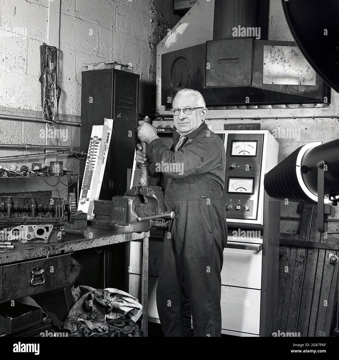 1970s, historical, inside a car repair workshop, at a workbench using a vice, an elderly garage mechanic in overalls working on a shock absorber or damper for a car's suspension, England, UK. Stock Photo