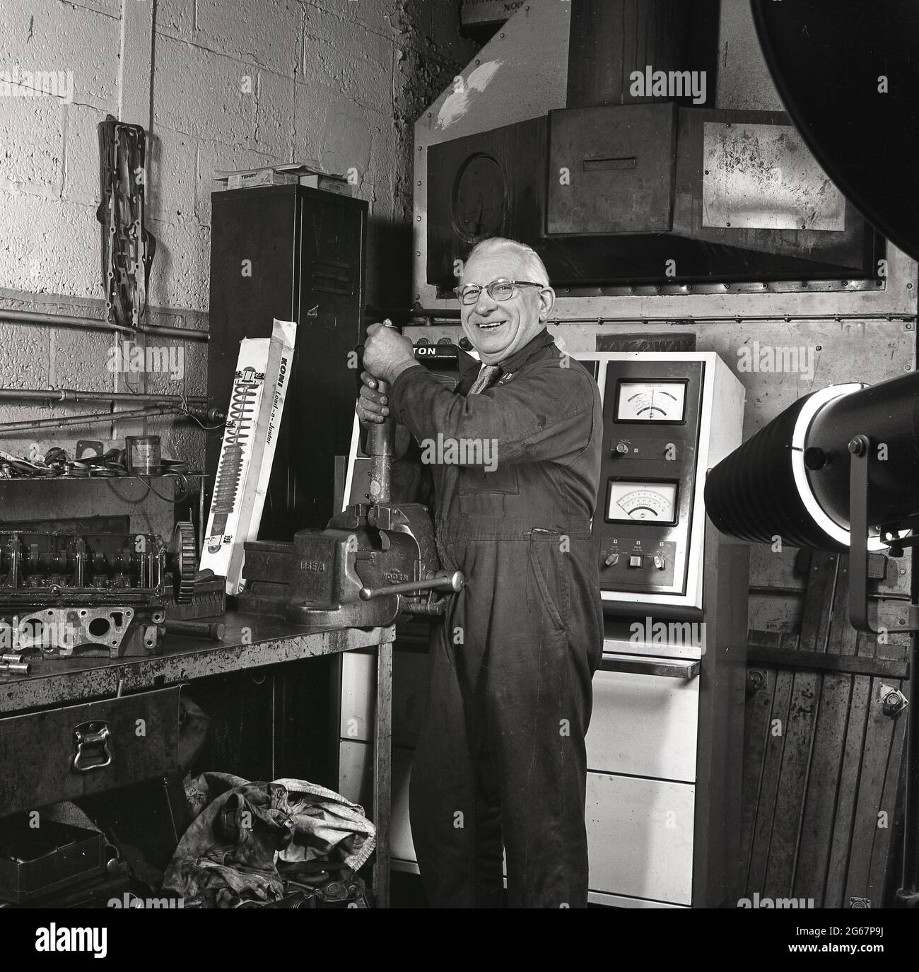 1970s, historical, inside a car repair workshop, at a workbench using a vice, an elderly garage mechanic in overalls working on a shock absorber or damper for a car's suspension, England, UK. Stock Photo