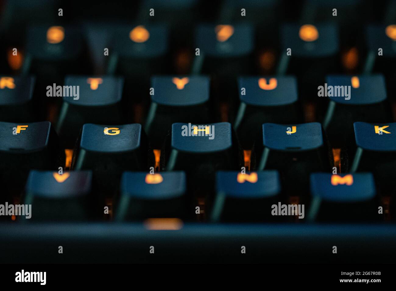 Orange coloured LED keys on a black keyboard. The letters G, H and J are prominantly in focus. Stock Photo