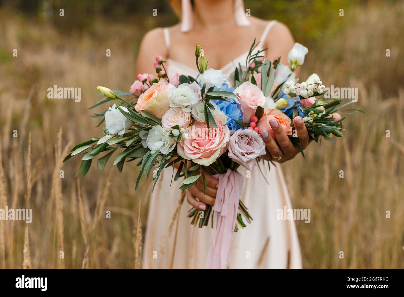 A delicate and very beautiful wedding bouquet of roses, greenery, eustoma and hydrangea in brides hands. Bridal trendy florists in pastel colors. Hand Stock Photo