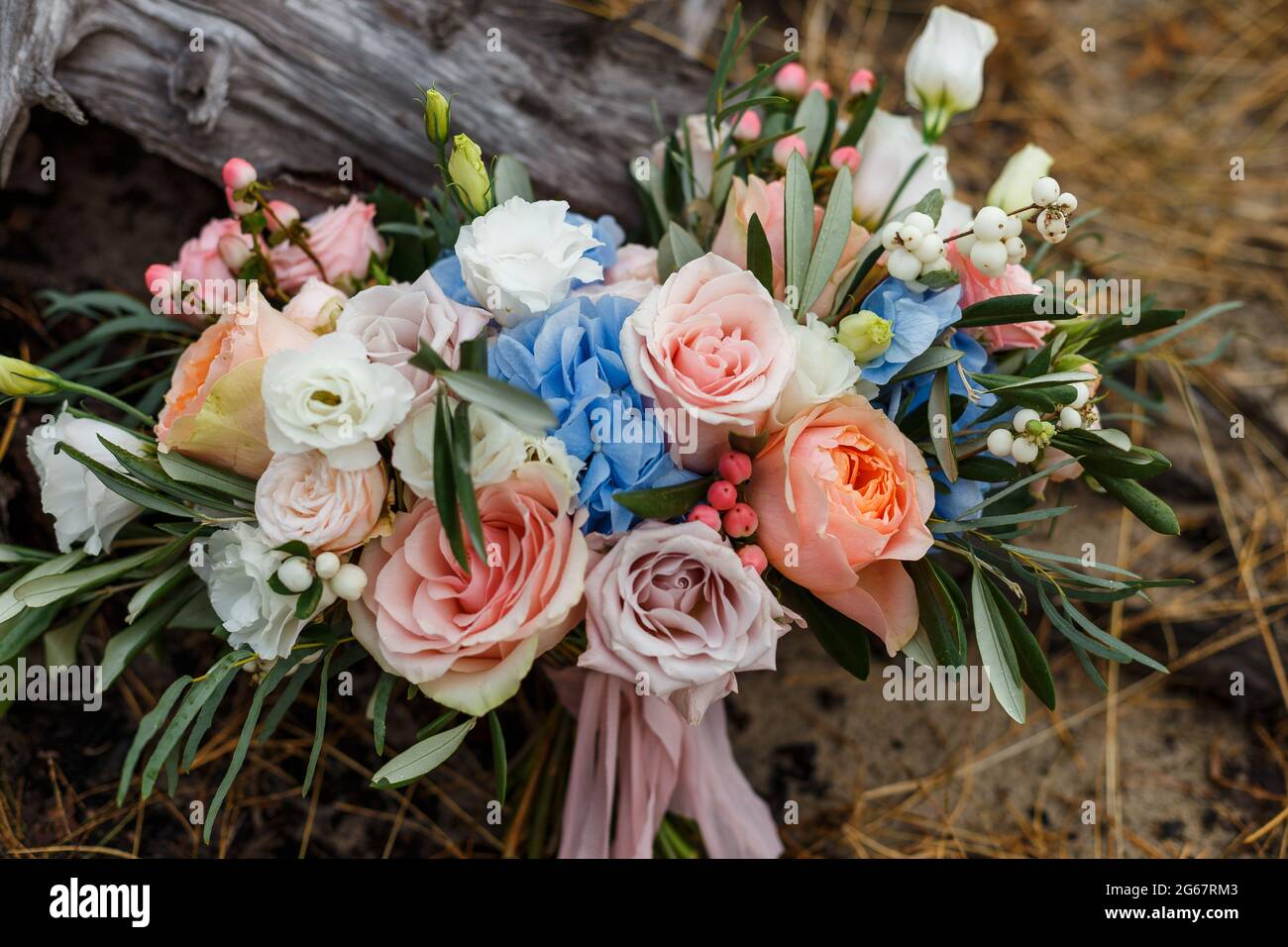 A delicate and very beautiful wedding bouquet of roses, greenery, eustoma and hydrangea on a background of dry stump. Bridal trendy florists in pastel Stock Photo
