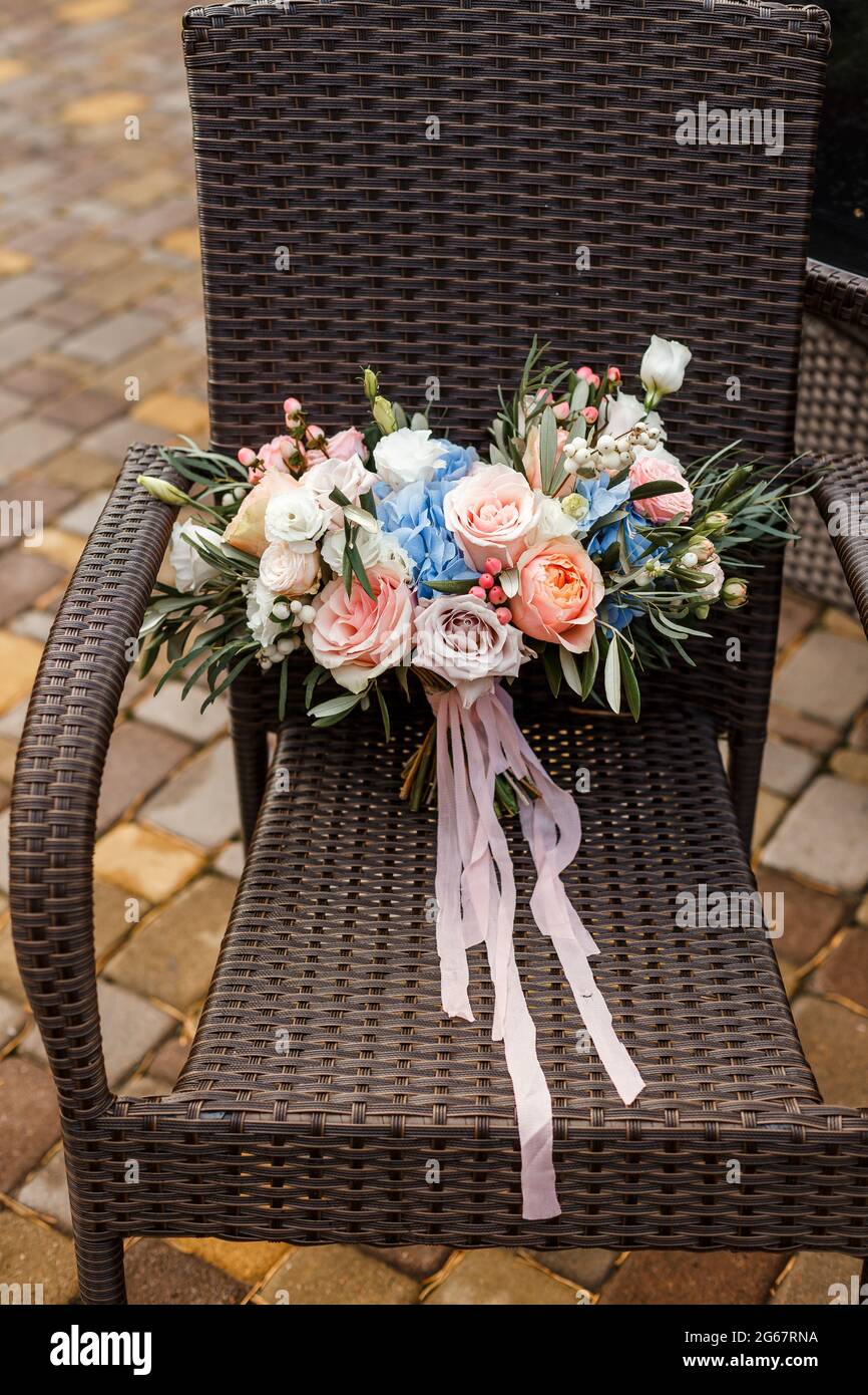 A delicate and very beautiful wedding bouquet of roses, greenery, eustoma and hydrangea on a background of chair. Bridal trendy florists in pastel col Stock Photo