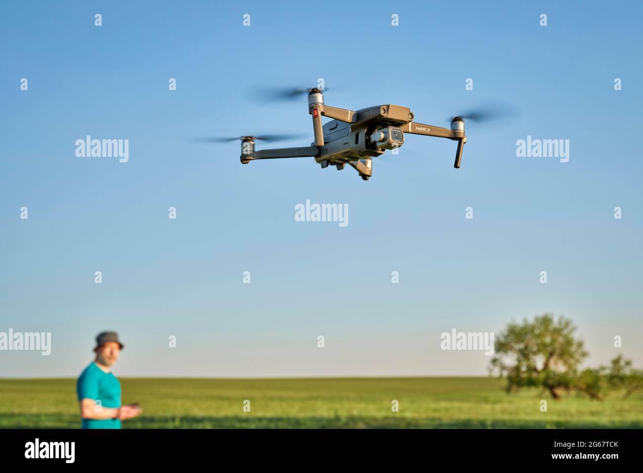 Briggsdale, CO, USA - June 8, 2021:  Radio controlled DJI Mavic 2 Pro quadcopter drone is flying over green prairie with a out of focus male pilot in Stock Photo