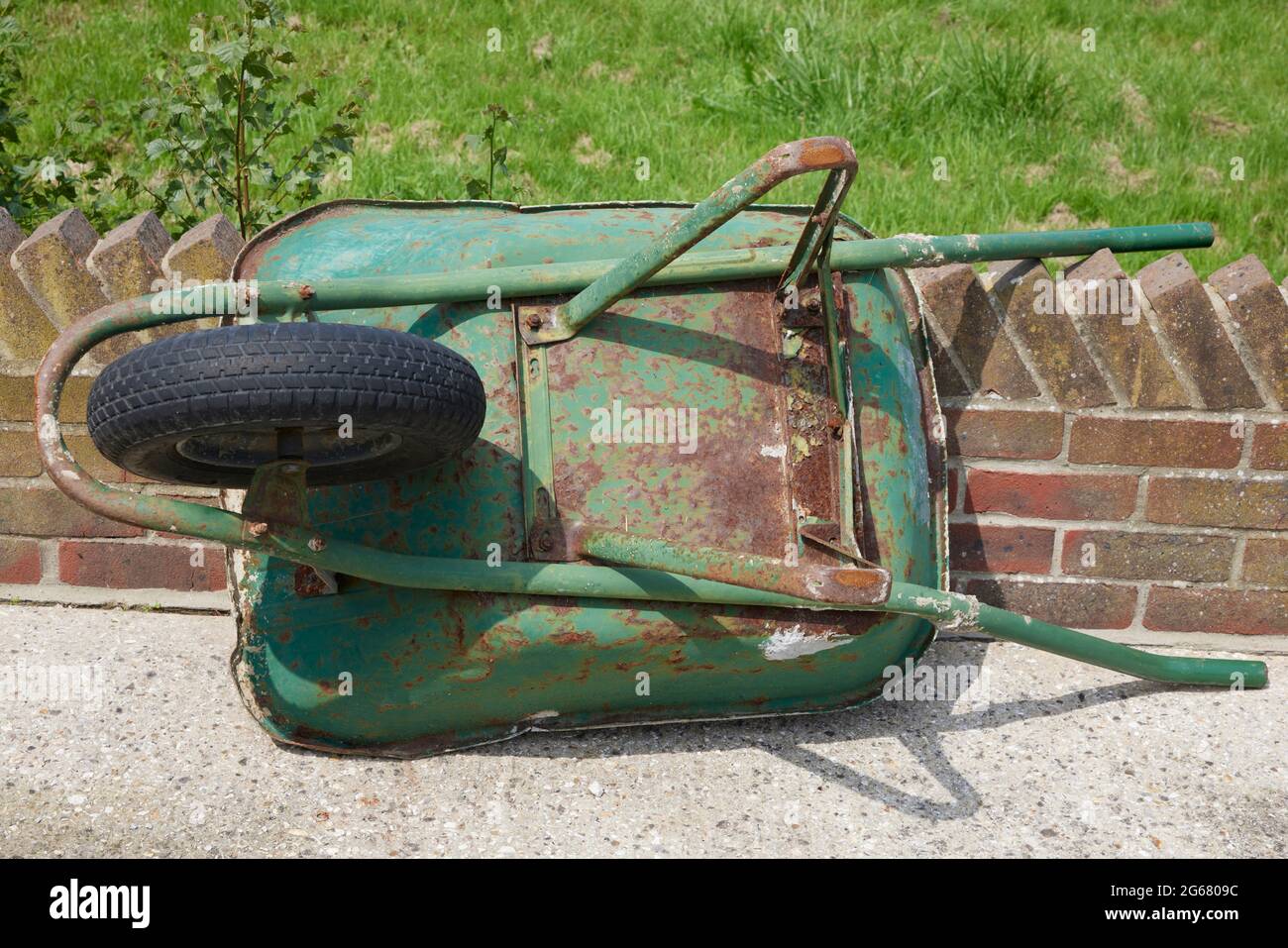 Used wheelbarrow seen discarded against a wall. Stock Photo