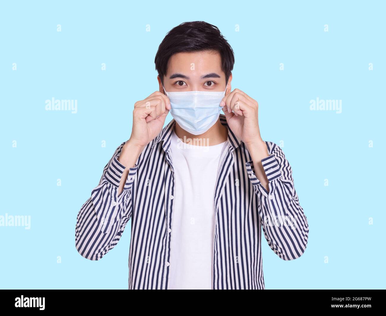 The handsome young man wears a protective medical mask to prevent COVID-19 infection and touches the mask for inspection. Stock Photo