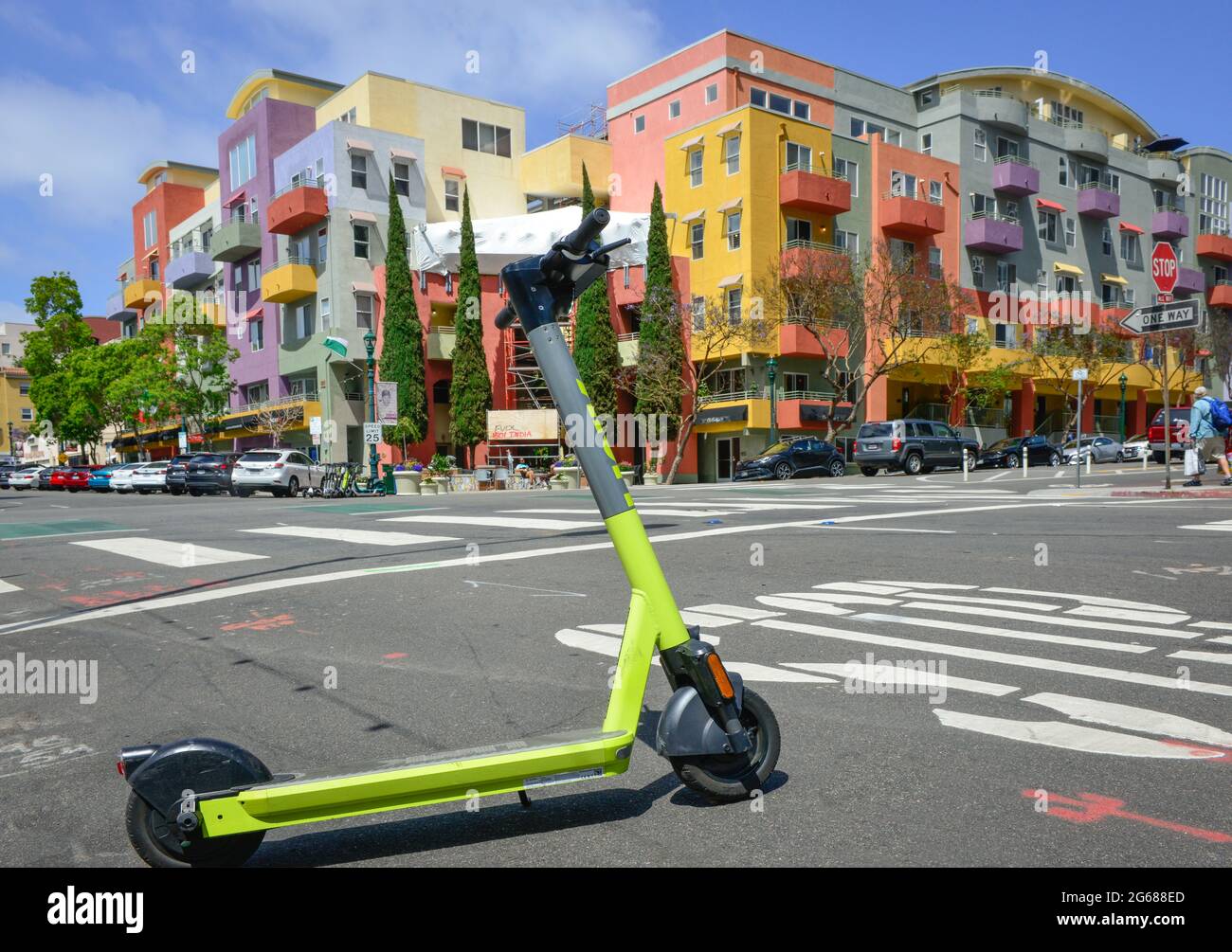A lime colored app-based rental scooter parked across from the modern San Diego Village Walk Condominiums, India Street in Little Italy, San Diego, CA Stock Photo