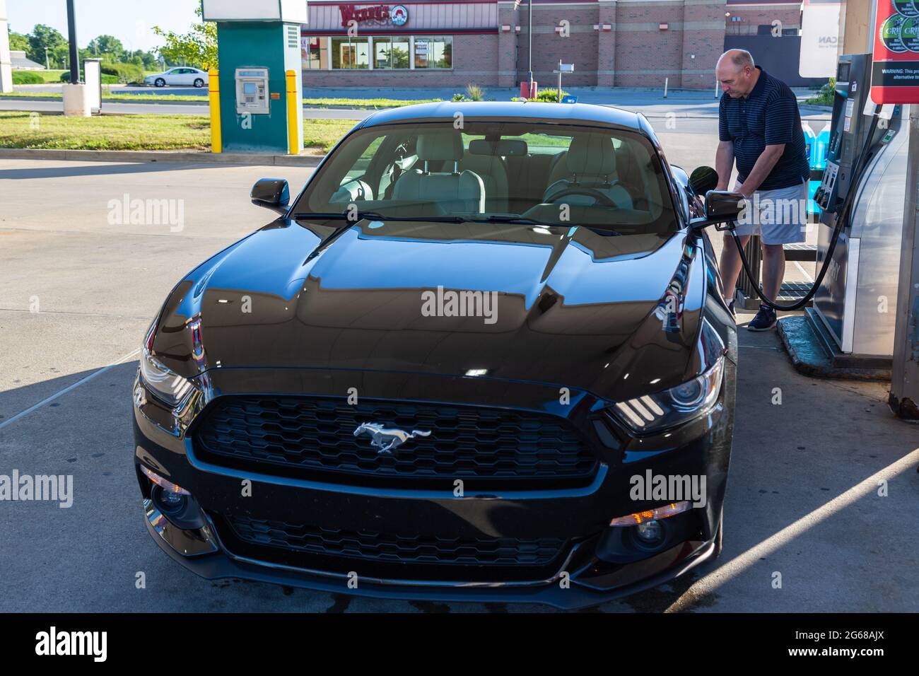 A man pumps gasoline into a black 2015 Ford Mustang at a Murphy USA gas station in Fort Wayne, Indiana, USA. Stock Photo