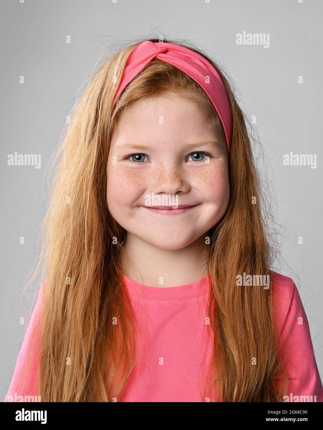 Portrait of happy smiling redhead kid girl with freckles on face in pink t-shirt and headband Stock Photo