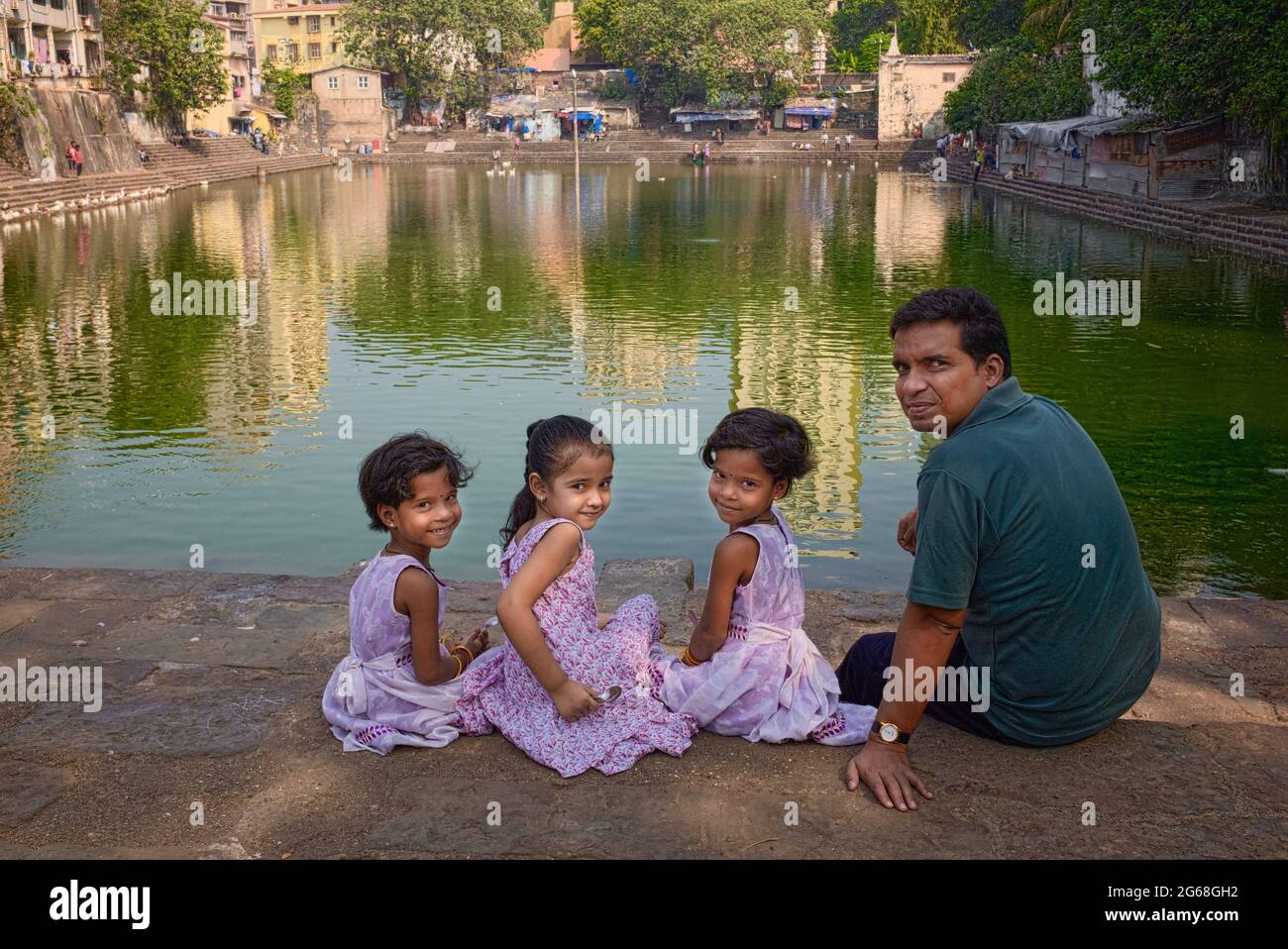A Hindu man with two young daughters and a niece sitting by sacred Banganga Tank, a Hindu pilgrimage site in Walkeshwar, Mumbai (Bombay), India Stock Photo