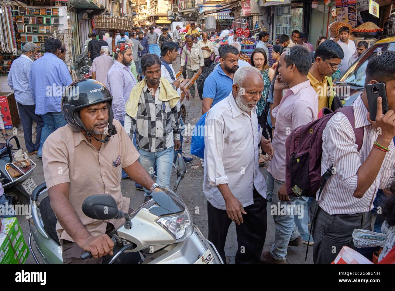 During the late afternoon rush, a motorcyclist drives through the through a throng of people in a lane in Zaveri Bazar, Mumbai (Bombay), India Stock Photo