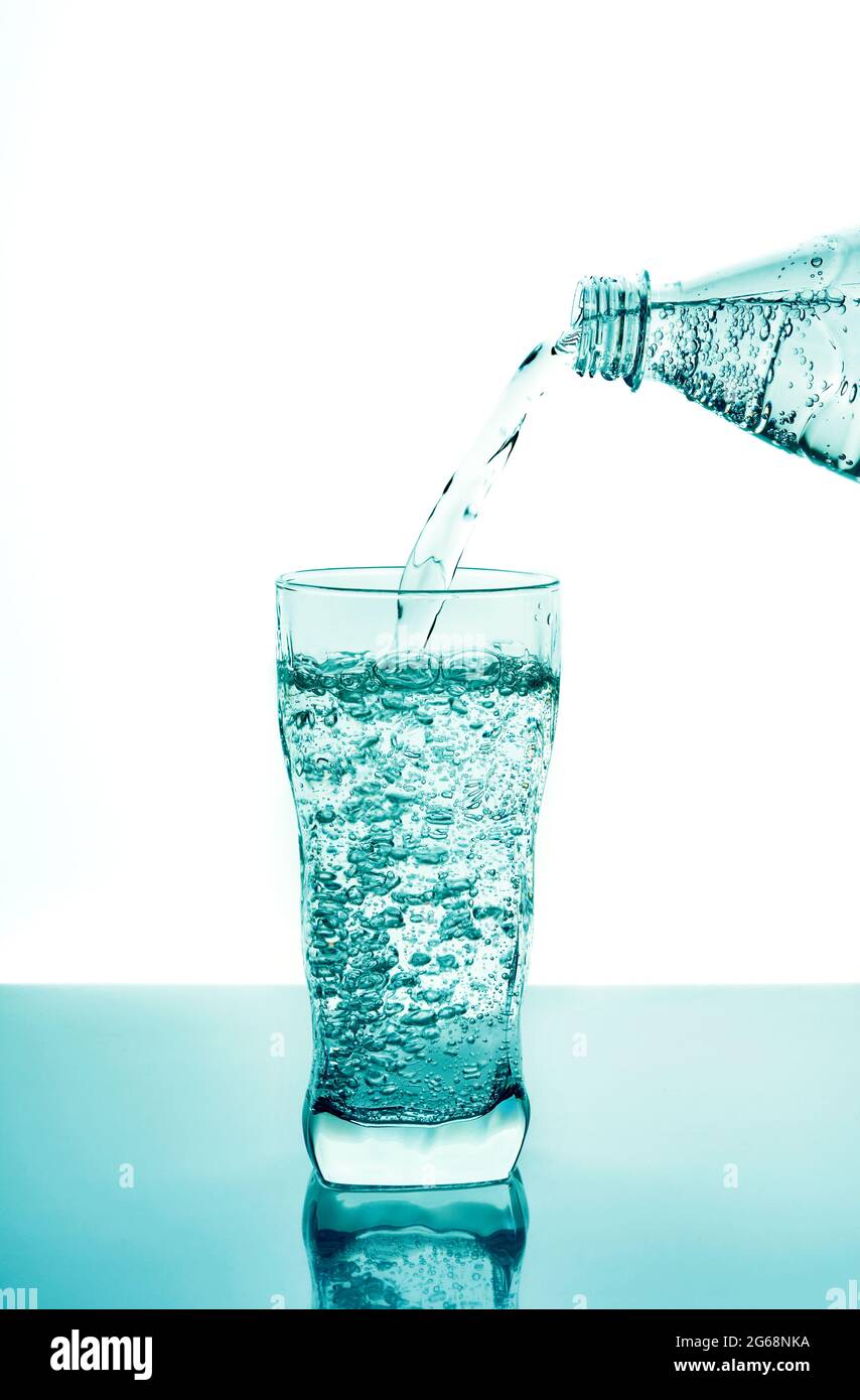 Pouring fresh water in glass from plastic bottle on blue background