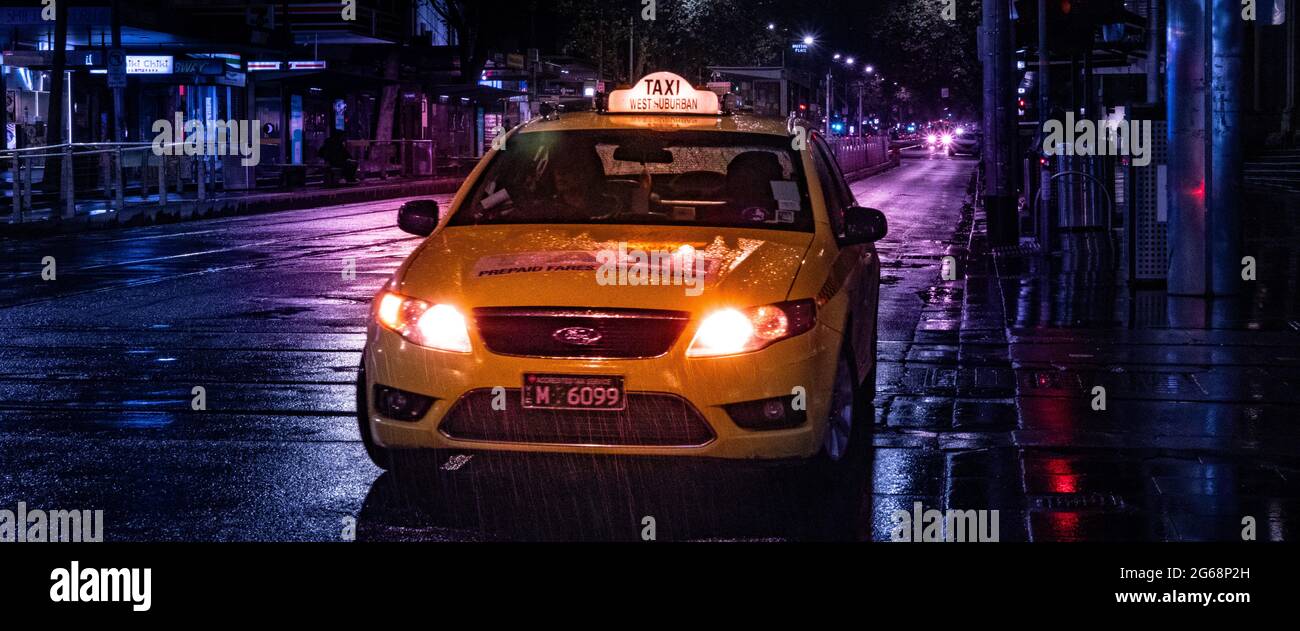 A Melbourne City yellow taxi cab on a rainy night with wet streets and light glows Stock Photo