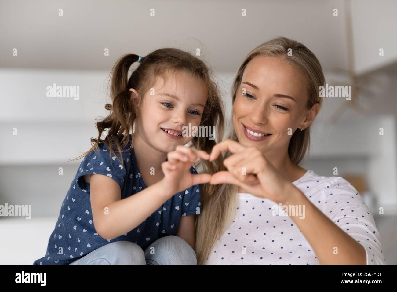 Smiling loving mother with adorable little daughter showing heart gesture Stock Photo