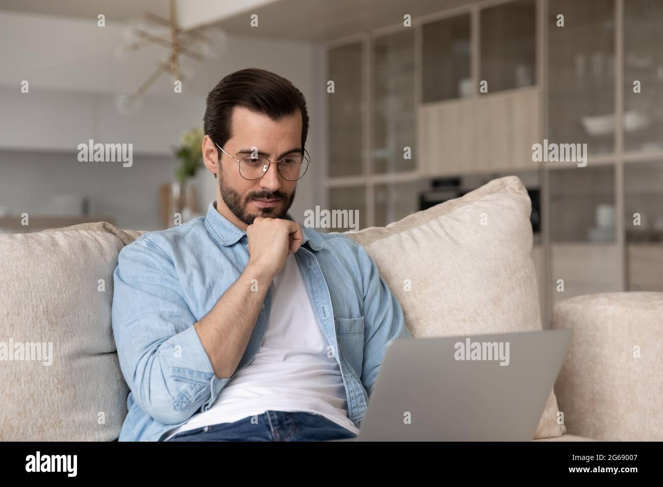 Thoughtful man in glasses looking at laptop screen, working online Stock Photo
