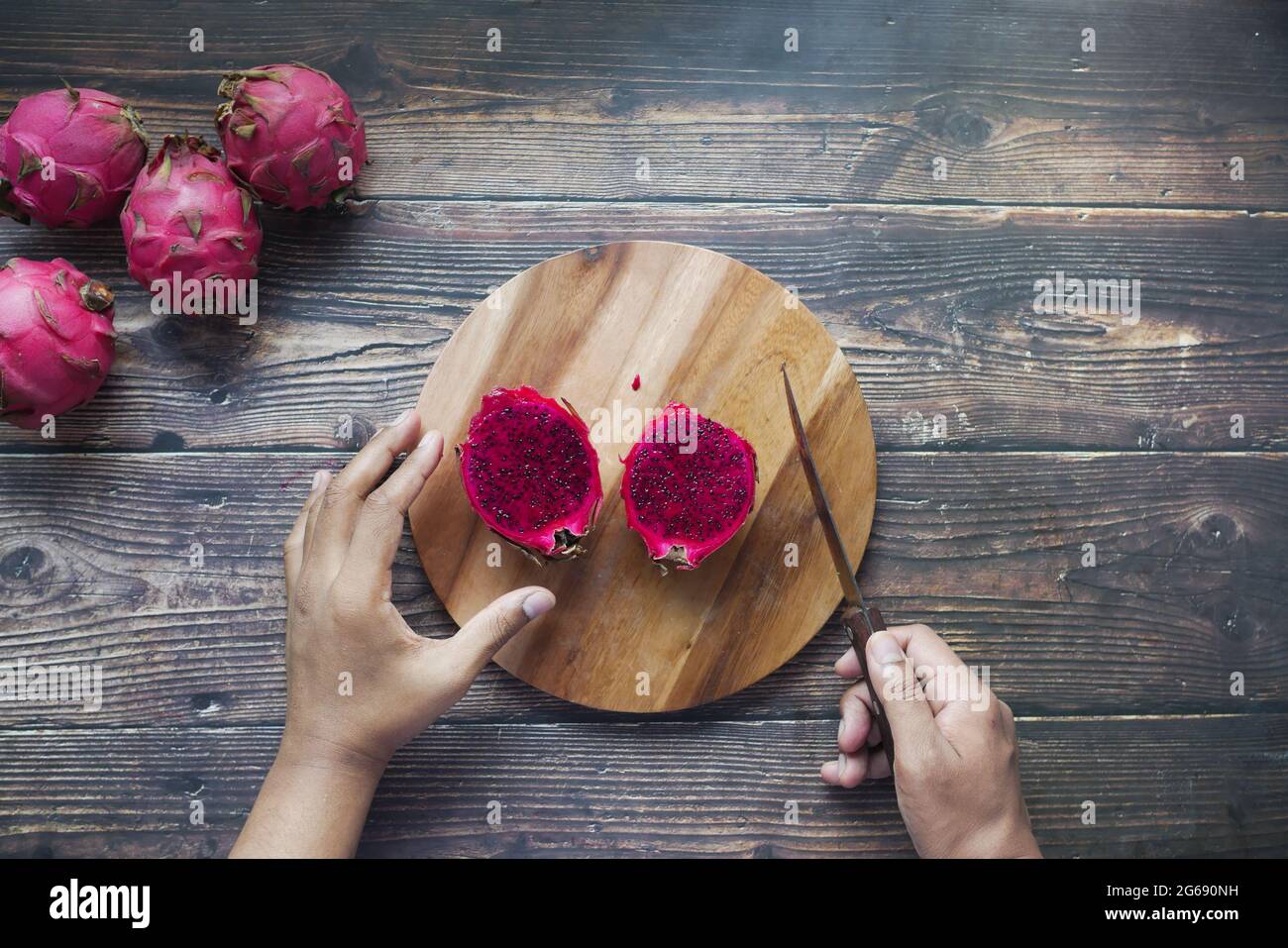 young man cutting a dragon fruit on a chopping board. Stock Photo