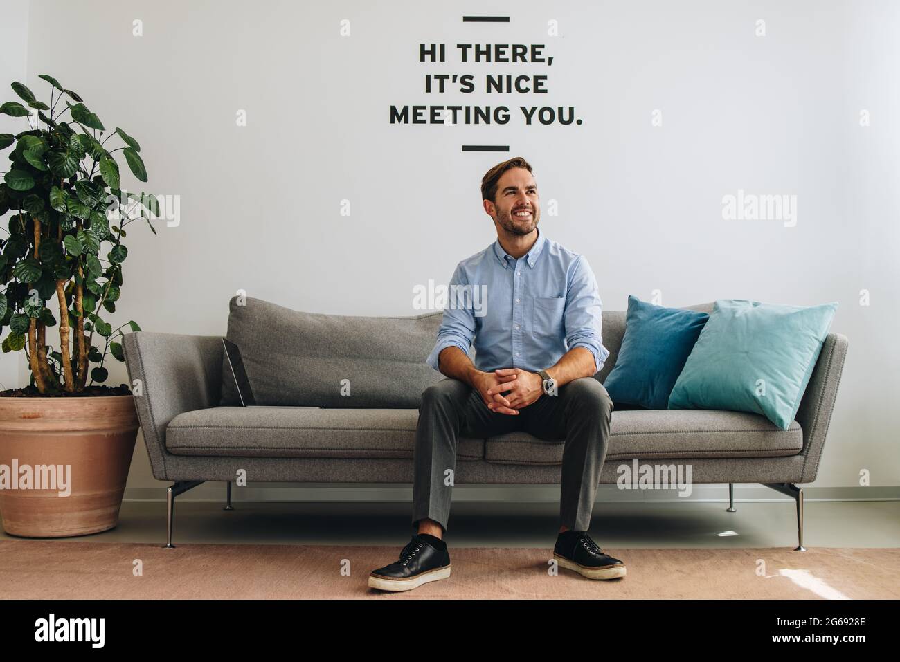 Entrepreneur at lobby, thinking of future plan. Man looking away and smiling on sofa at lobby. Stock Photo