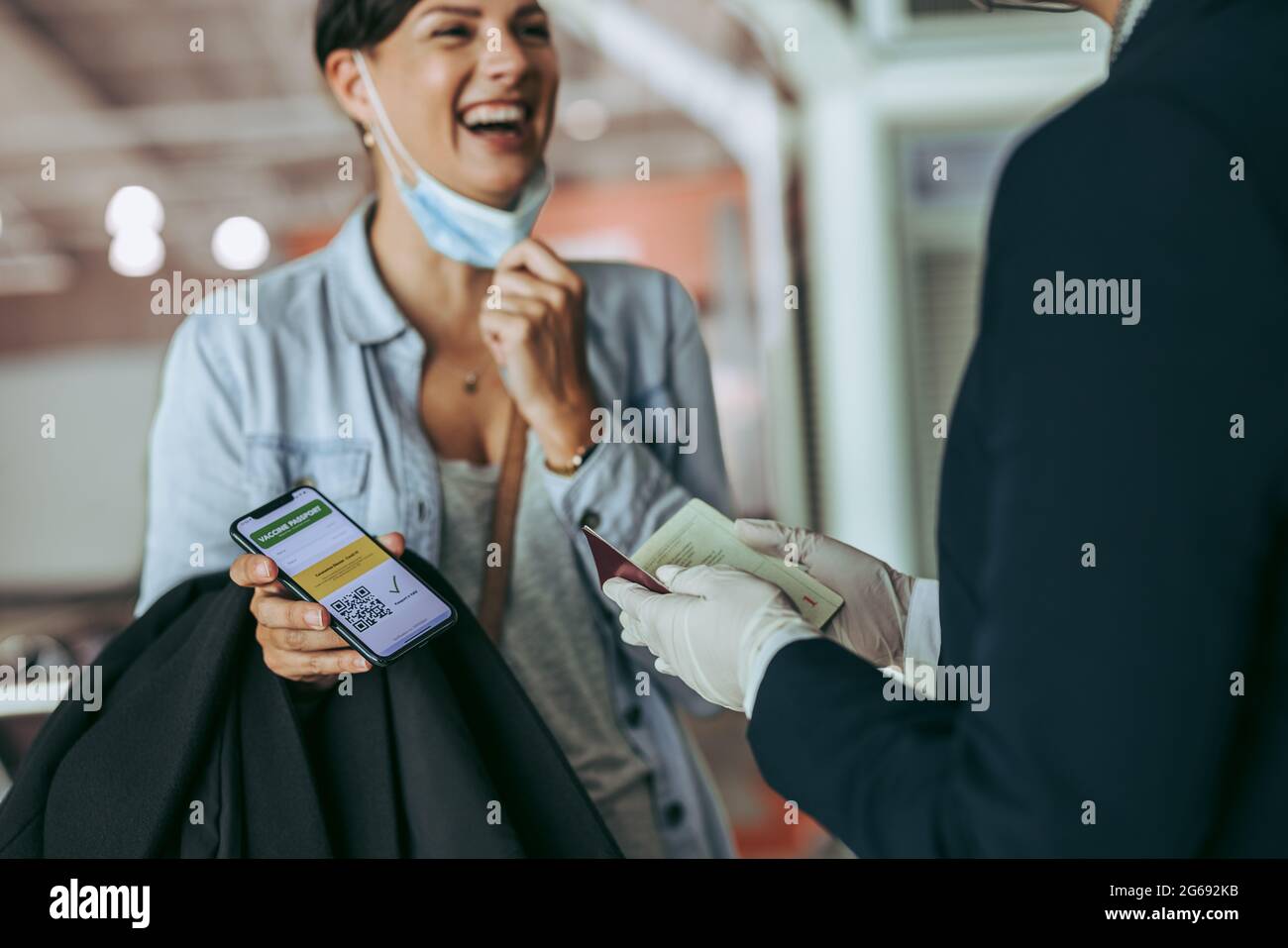 Woman traveler showing vaccine passport at check-in counter of airport. Female at checking counter displaying corona virus vaccine passport. Stock Photo