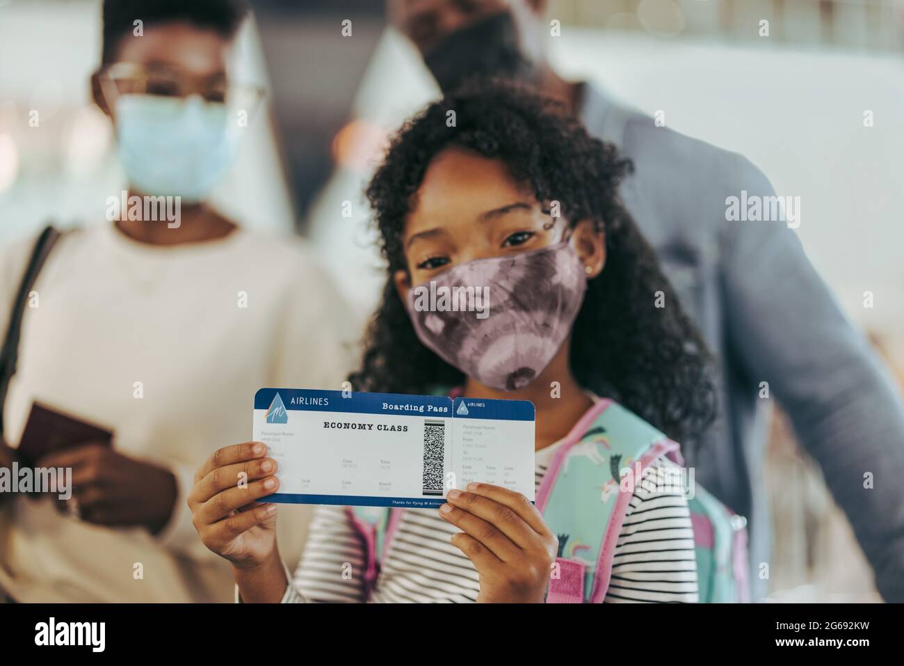 Girl showing boarding pass while at boarding gate with family. Young girl and her family at airport doing on a holiday during pandemic. Stock Photo