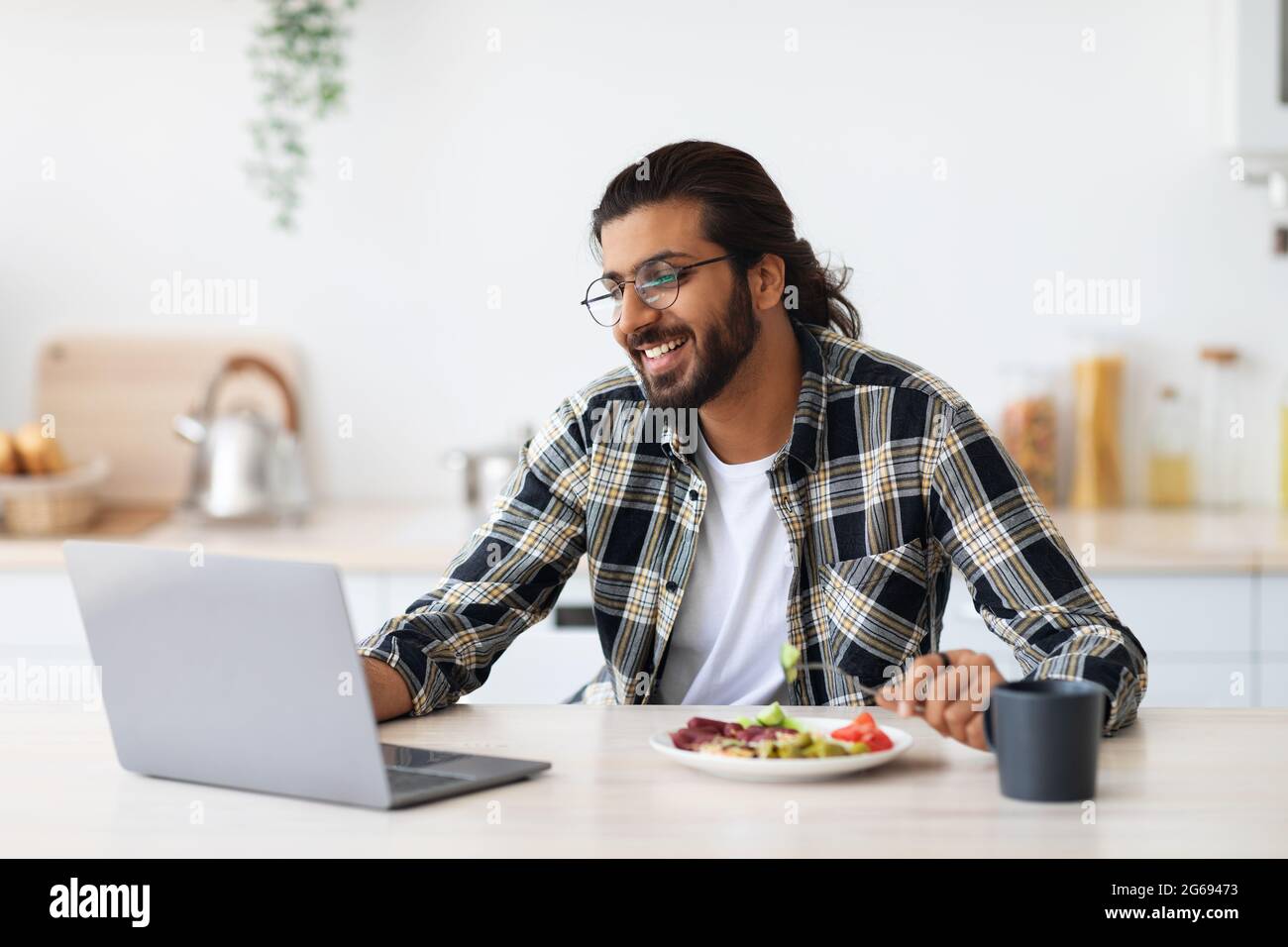 Cheerful middle-eastern guy having snack while working from home Stock Photo